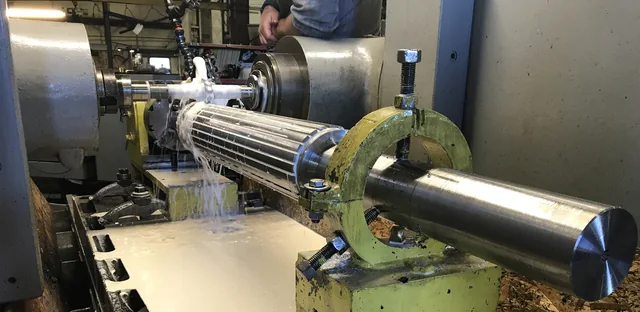 Long grooved metal roller held between sections of shop machinery