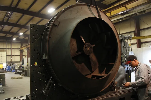 Worker beside a large round metal workpiece in the shop