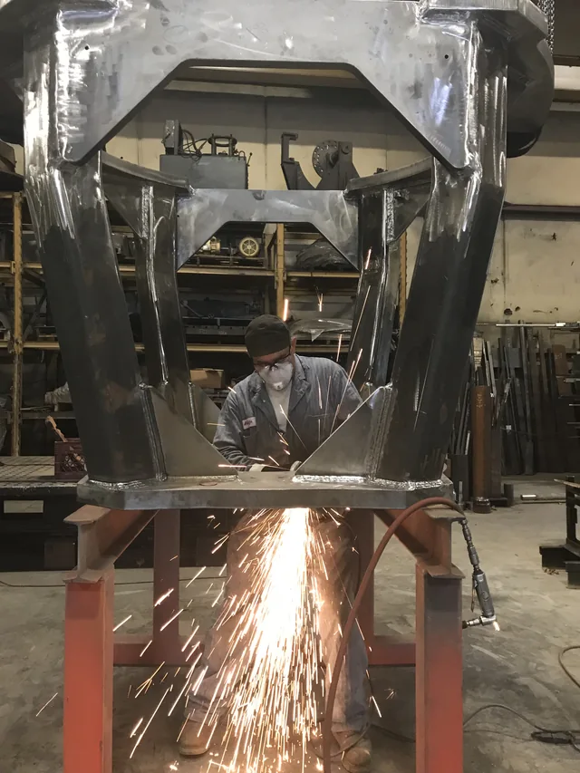 Sparks falling beneath a large metal frame in the shop